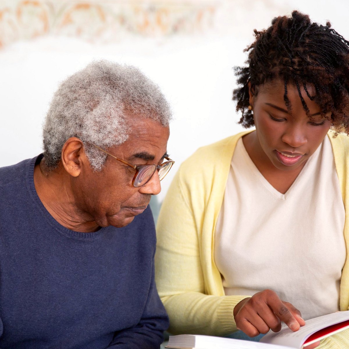Care worker reading with an older man on a sofa at home