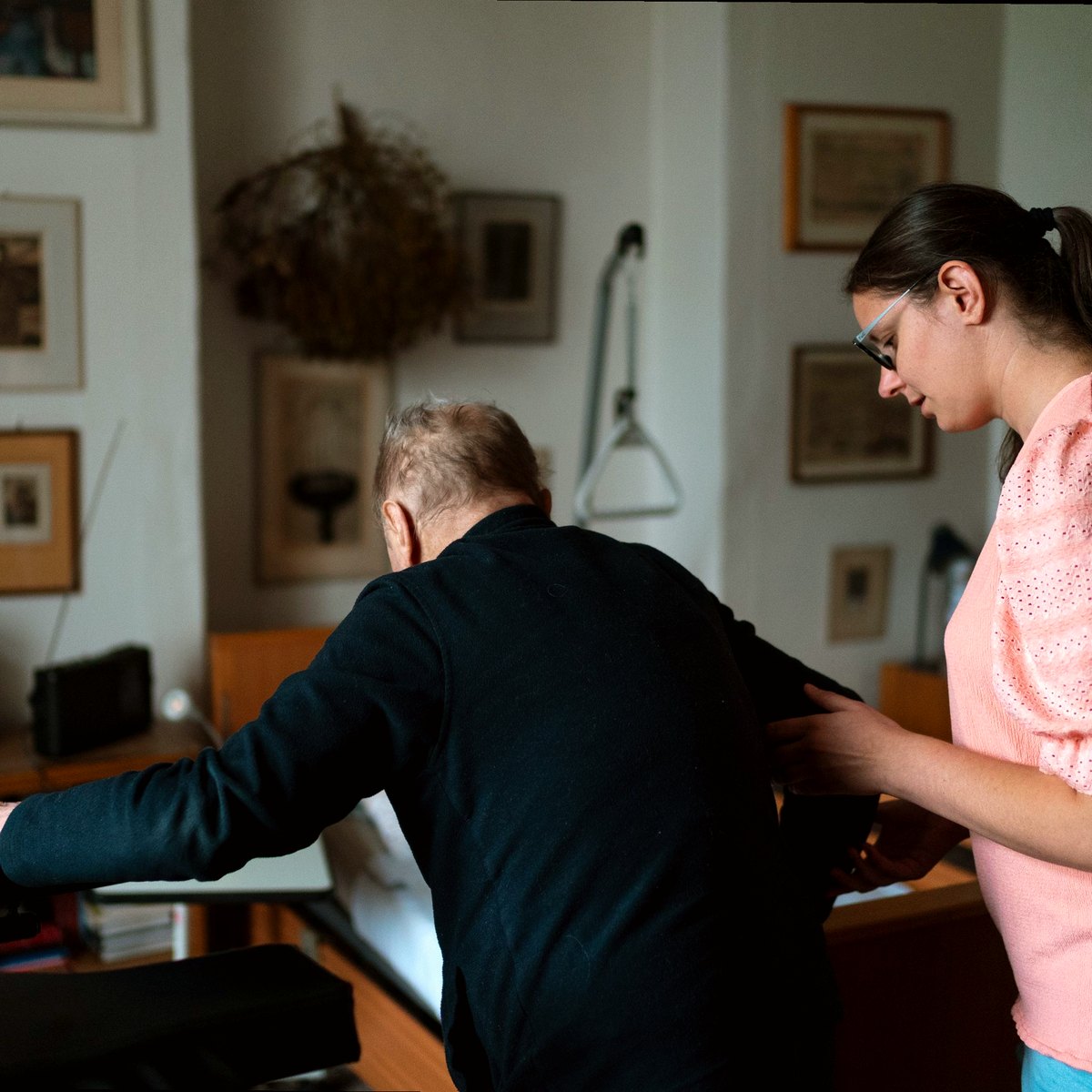 Care worker helping an older man stand in his living room